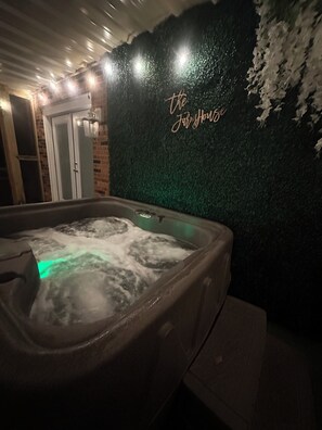 A hot tub with a green wall and a neon sign that reads "the Jolly House."
