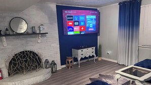 Ein modernes Wohnzimmer mit Flachbildfernseher an der Wand, einem Kamin, einem blauen Sofa und einem kleinen Beistelltisch.