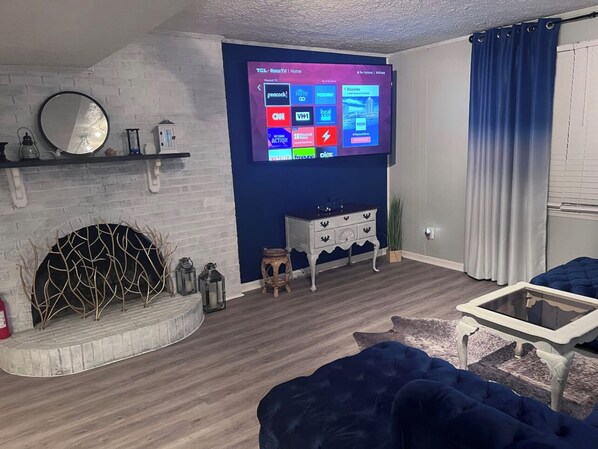 Una sala de estar moderna con un televisor de pantalla plana montado en la pared, una chimenea, un sofá azul y una mesita auxiliar.