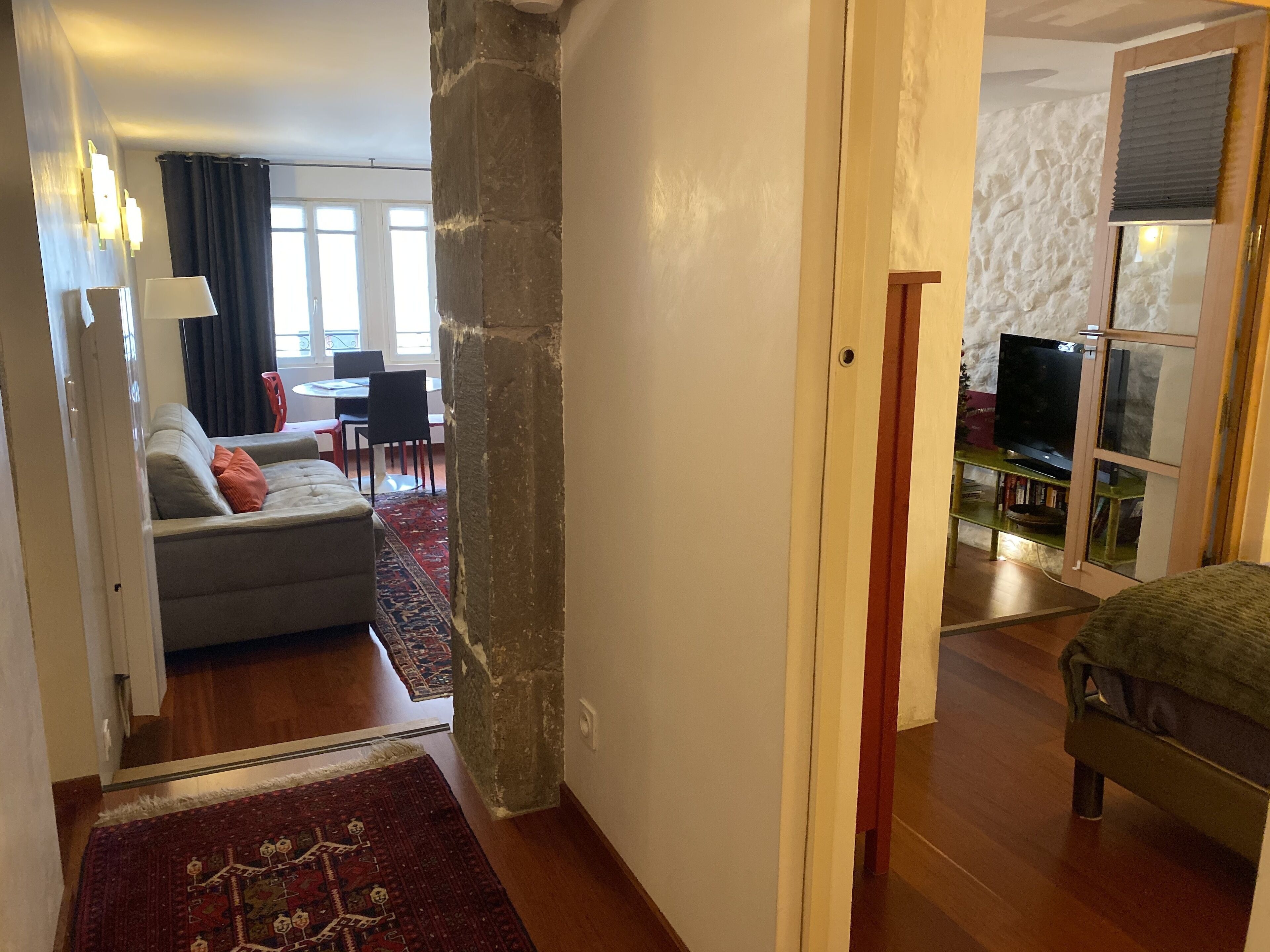 Sala de estar con sofá, una mesa de centro y mueble para televisión. Hay un comedor con una mesa y sillas. La habitación tiene piso de madera y una alfombra roja.