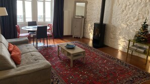 A living room with a sofa, a coffee table, a patterned rug, a dining area with chairs, a fireplace, and a Christmas tree. - Les Rêveries-beautiful apartment in the heart of the historic center (Annecy)