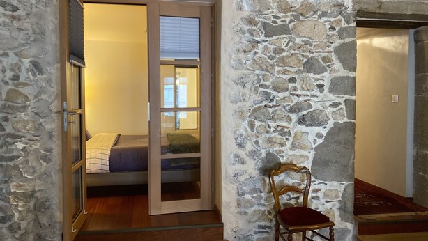 A room with a stone wall, a wooden chair, and a bed with a blue blanket. - Les Rêveries-beautiful apartment in the heart of the historic center (Annecy)