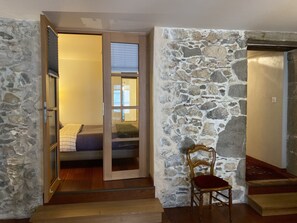A room with a stone wall, a wooden chair, and a bed with a blue blanket. - Les Rêveries-beautiful apartment in the heart of the historic center (Annecy)