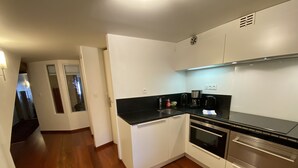 A modern kitchen with white cabinets, a black countertop, stainless steel appliances, and a wooden floor. - Les Rêveries-beautiful apartment in the heart of the historic center (Annecy)