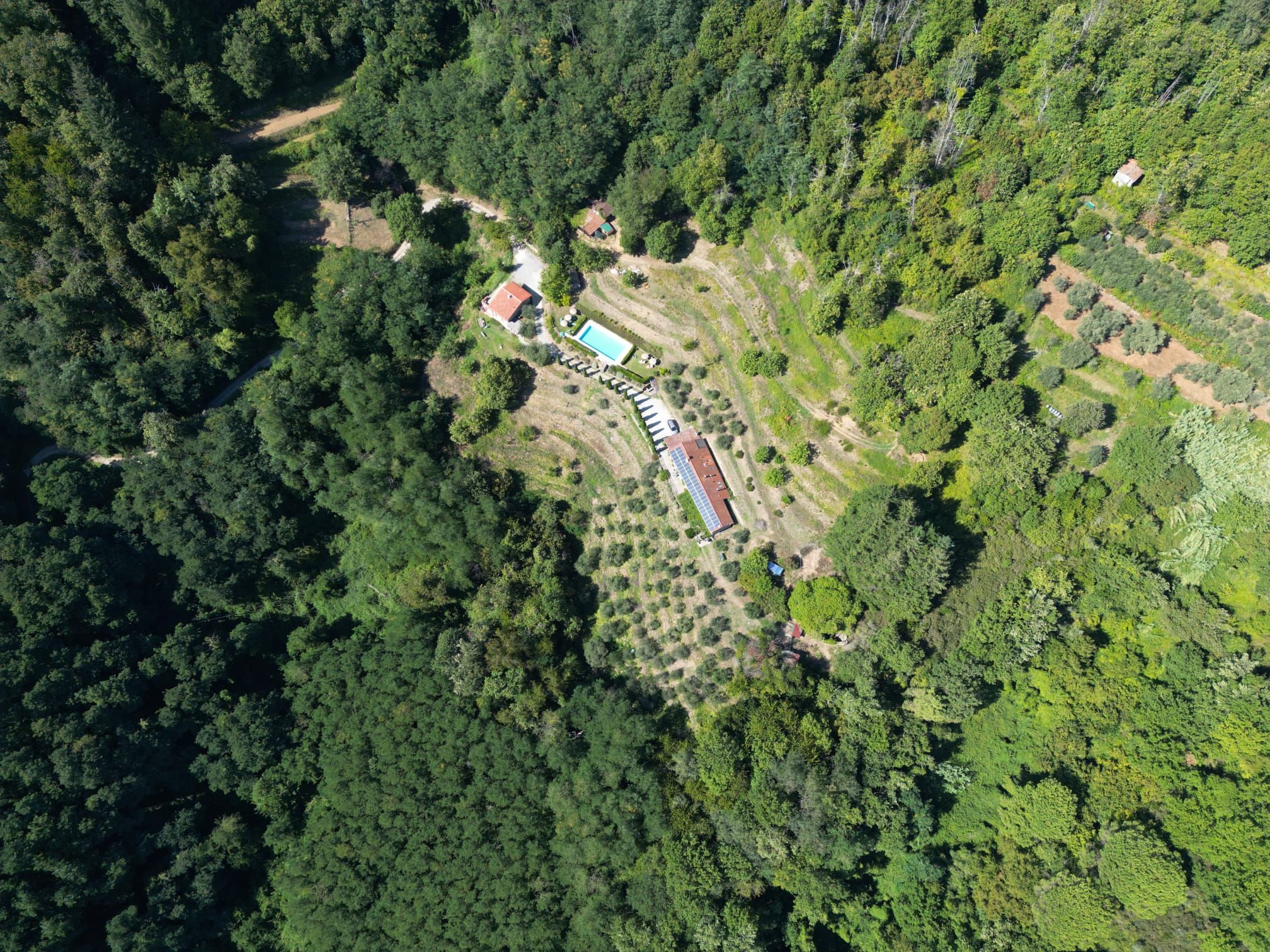 An aerial view of a property with a swimming pool, a tennis court, and a large building with a red roof.