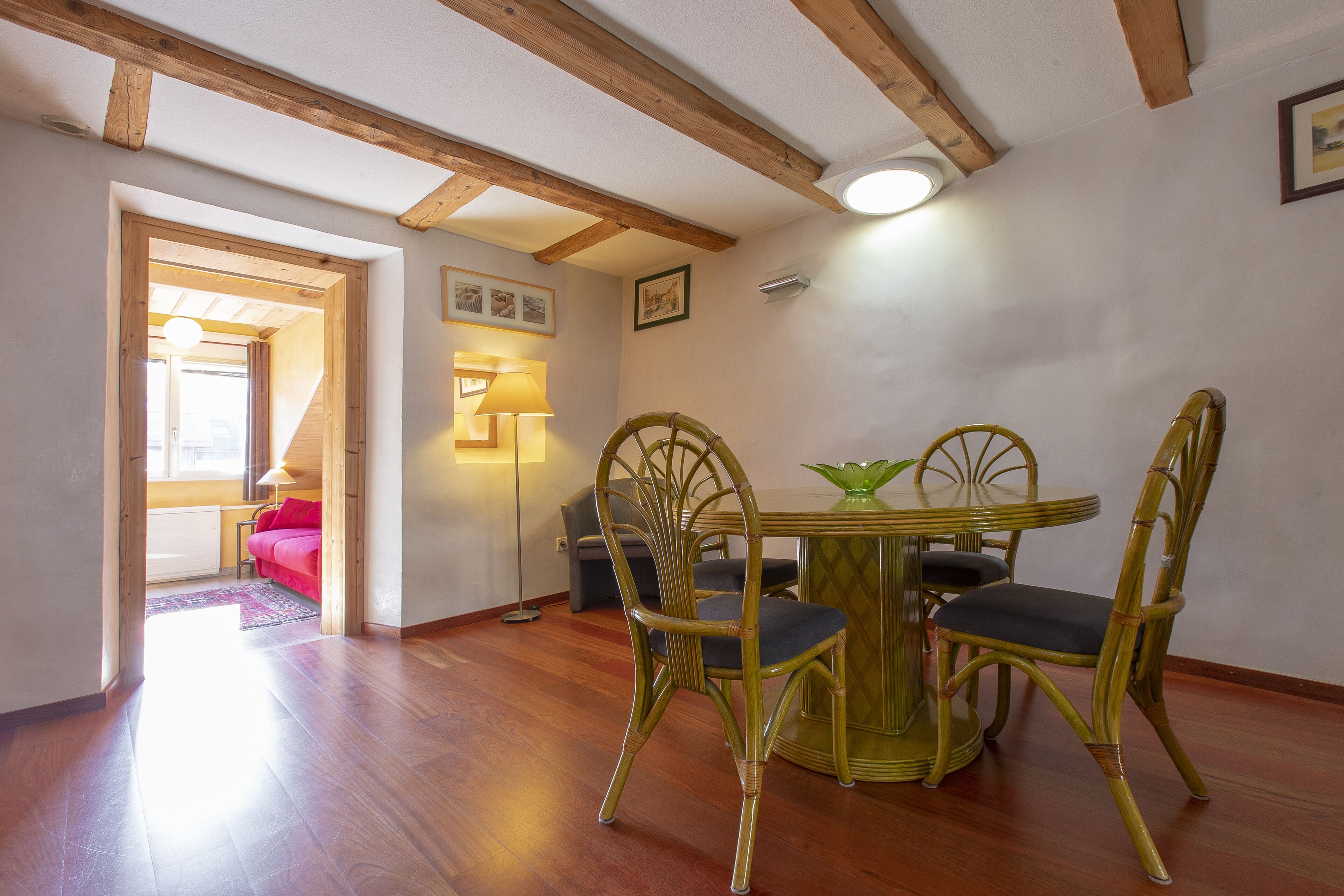 Un'area pranzo con un tavolo rotondo e quattro sedie, travi in legno al soffitto e un'apertura che dà su un'altra stanza.