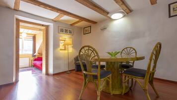 Un'area pranzo con un tavolo rotondo e quattro sedie, travi in legno al soffitto e un'apertura che dà su un'altra stanza.