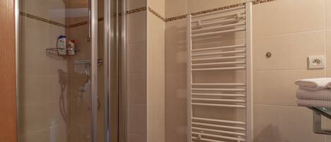 A bathroom with a glass shower enclosure, a white towel rack, and a tiled wall with a decorative border.