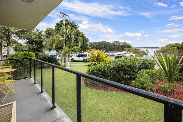 A balcony with a view of a parking area, greenery, and a body of water. - Wallis View 3 - Short stroll to beaches and restaurants (Forster)