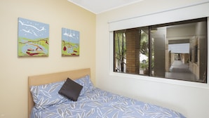 Ein Schlafzimmer mit einem Bett, einem Fenster und zwei an der Wand befestigten Bildern.
