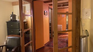 Hotelkamer met een houten plafond, een bureau met koffiezetapparaat, een stoel, een radiator en een raam met uitzicht op de gang.