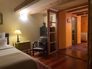 A cozy room with a bed, a chair, a desk with a lamp, and a wardrobe.
