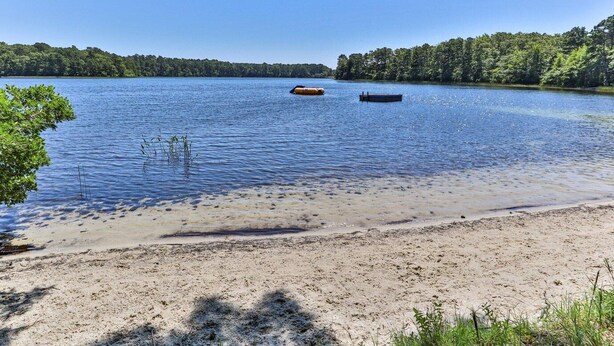 A sandy beach with calm water, a boat, and a forested shoreline. - Family Oasis in Great Location with Pool (Harwich)