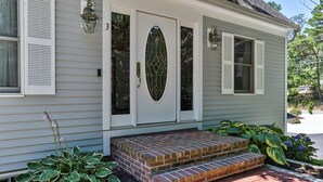A house with a front door, a brick step, and a small garden with plants. - Family Oasis in Great Location with Pool (Harwich)