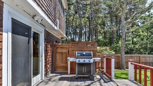 A deck with a grill, a sliding glass door, and a wooden fence. - Family Oasis in Great Location with Pool (Harwich)