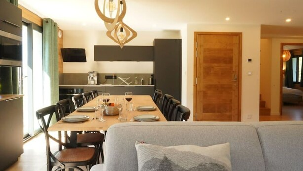 Un comedor moderno con una mesa de madera preparada para seis personas, rodeada de sillas. Una lámpara colgante original ilumina la mesa.