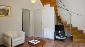 A living room with a white sofa, a wooden coffee table, a painting on the wall, and a staircase with wooden steps and metal railings.
