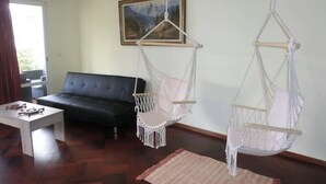 Ein Wohnzimmer mit einer schwarzen Couch, einem weißen Couchtisch und zwei Hängestühlen aus Makramee.