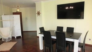 Ein Essbereich mit einem schwarzen Tisch und Stühlen, einem an der Wand befestigten Flachbildfernseher und Holzboden.