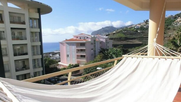 Eine Hängematte auf einem Balkon mit Blick auf eine Küstenlandschaft, Gebäude und eine Bergkulisse.