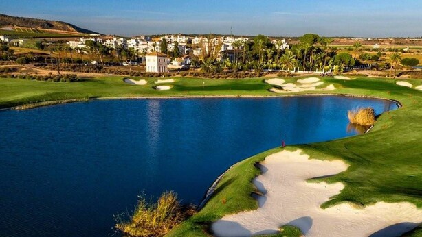 Un campo da golf con uno stagno, bunker di sabbia e una zona residenziale sullo sfondo.
