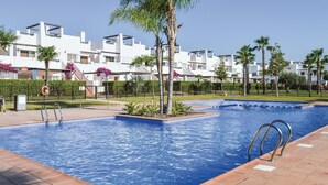 Una piscina con un galleggiante, circondata da palme e un edificio bianco con balconi.