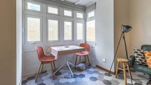 Une pièce comprenant une table et deux chaises, un lampadaire et un canapé vert agrémenté de coussins à motifs.