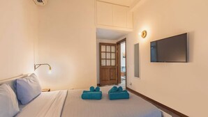 Une chambre à coucher avec un lit, un téléviseur fixé au mur et une porte donnant sur une autre pièce.