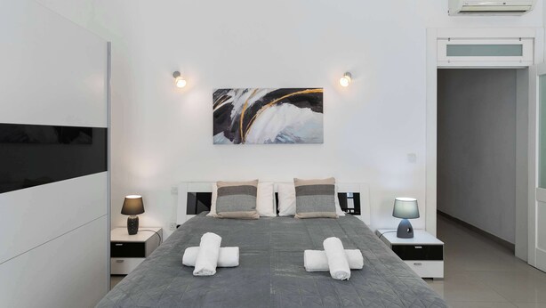 A modern hotel room with a large bed, two bedside tables with lamps, a wall-mounted air conditioner, and a painting above the bed. - 22 - Unique Four Bedroom Townhouse by PMI Malta (Tas-Sliema)