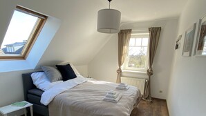 Ett sovrum med en säng, ett sängbord, ett litet bord, ett element, ett fönster med gardiner och en hängande lampa.