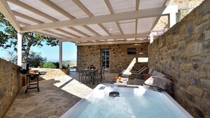 A stone patio with a hot tub, outdoor seating, and a grill.