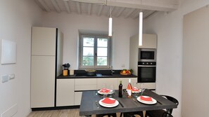 Uma cozinha moderna com armários brancos, bancada preta e uma mesa de jantar posta para dois, com guardanapos vermelhos e taças de vinho.