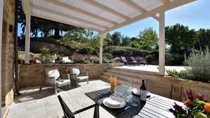Eine Terrasse im Freien mit Steinmauern, einem überdachten Sitzbereich und einem für das Essen gedeckten Tisch.