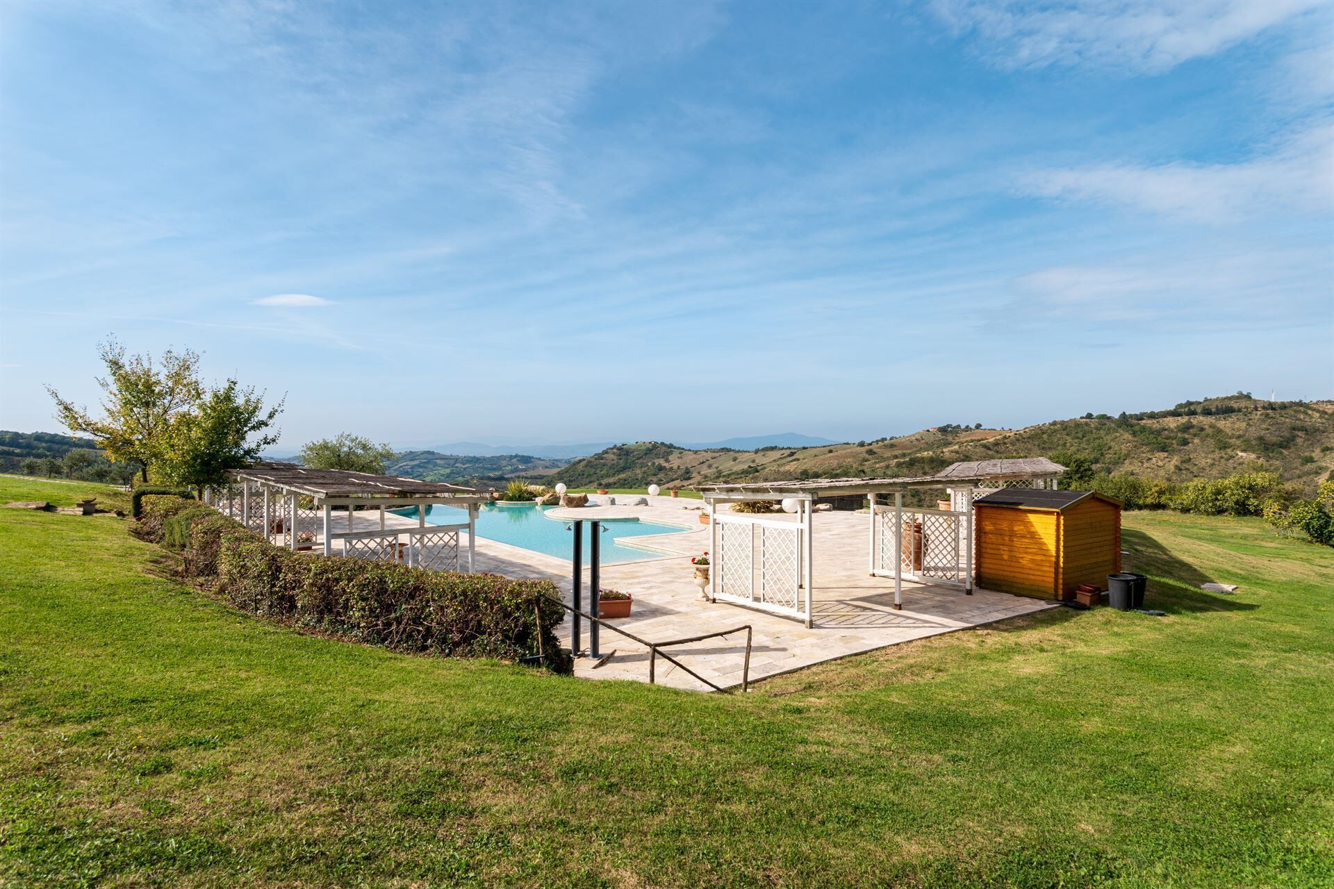 Zona de piscina con una pérgola, un cobertizo pequeño y vistas a colinas ondulantes.