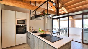 Cozinha moderna com ilha central, fornos embutidos e uma grande janela com vista para uma varanda.