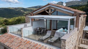 A modern villa with a glass-enclosed patio, a hot tub, and a dining area overlooking a mountainous landscape. - Ovile, Fattoria la Pieve, Roccalbegna, Grosseto and Maremma (Roccalbegna)
