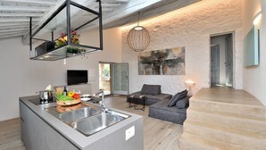 A modern kitchen with a central island, a dining area with a sofa, and a staircase leading to another level. - Pievania, Fattoria la Pieve, Roccalbegna, Grosseto and Maremma (Roccalbegna)