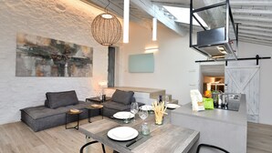 A modern living room with a sofa, coffee table, and dining area. There is a kitchen visible in the background. - Pievania, Fattoria la Pieve, Roccalbegna, Grosseto and Maremma (Roccalbegna)