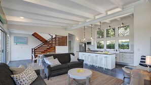 A spacious living area with a dark grey sofa, a round coffee table, and a staircase leading to an upper level. - The Ultimate Modern Straddie Beach House (Point Lookout)