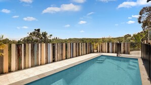 A rectangular swimming pool with a tiled deck, surrounded by a wooden fence and a metal gate. - The Ultimate Modern Straddie Beach House (Point Lookout)
