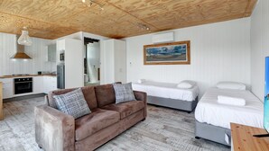 Ett mysigt rum med ett träpanelat tak, en soffa, två sängar, en tavla och en liten köksdel.