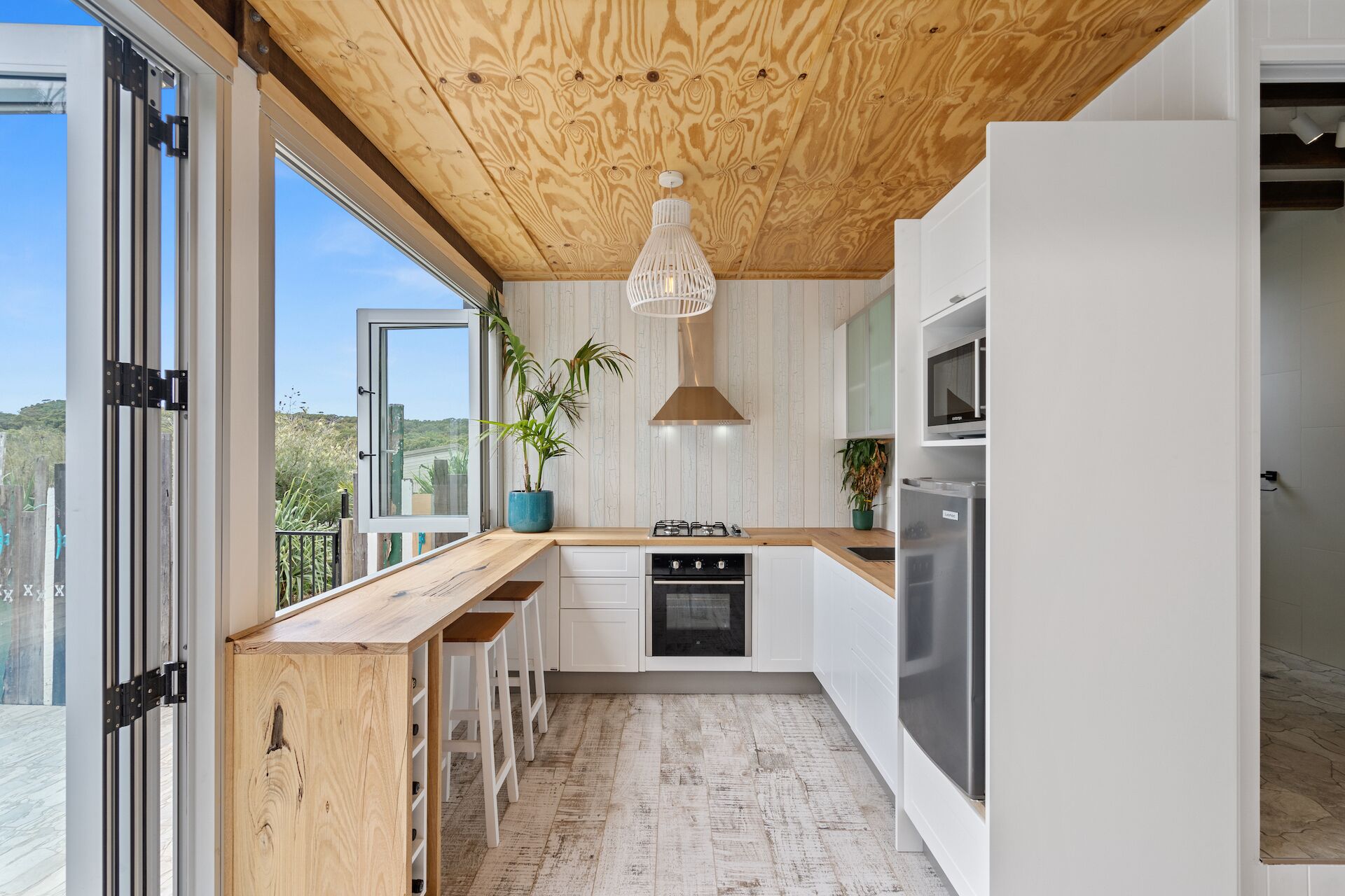 A modern kitchen with a wooden ceiling, white cabinets, and a large window.