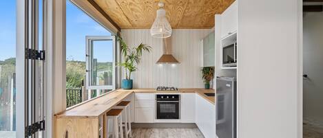 A modern kitchen with a wooden ceiling, white cabinets, and a large window.