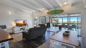 A modern living room with a TV, sofa, and dining area. - The Ultimate Modern Straddie Beach House (Point Lookout)