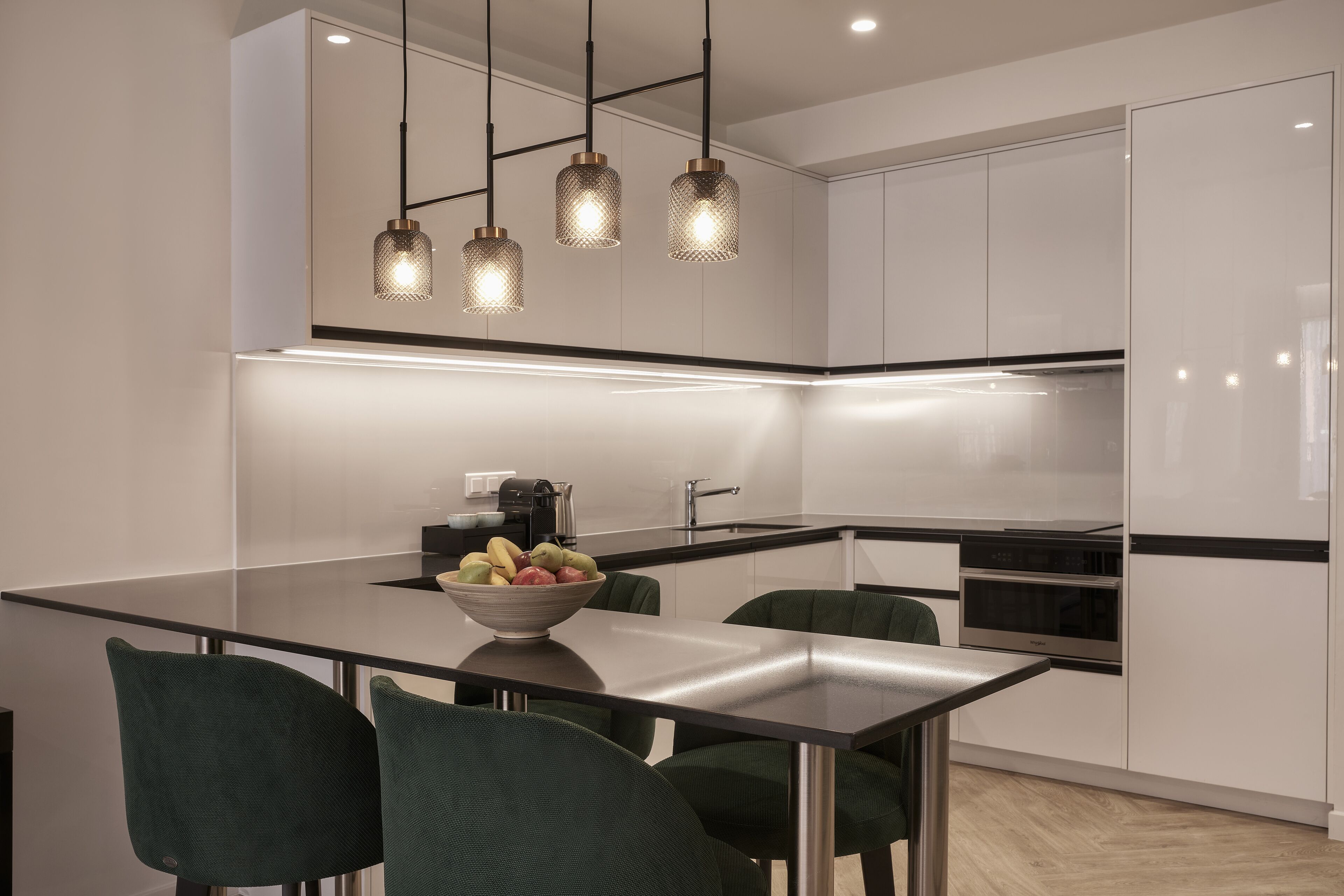 Una cocina moderna con una isla central, sillas verdes y lámparas colgantes.