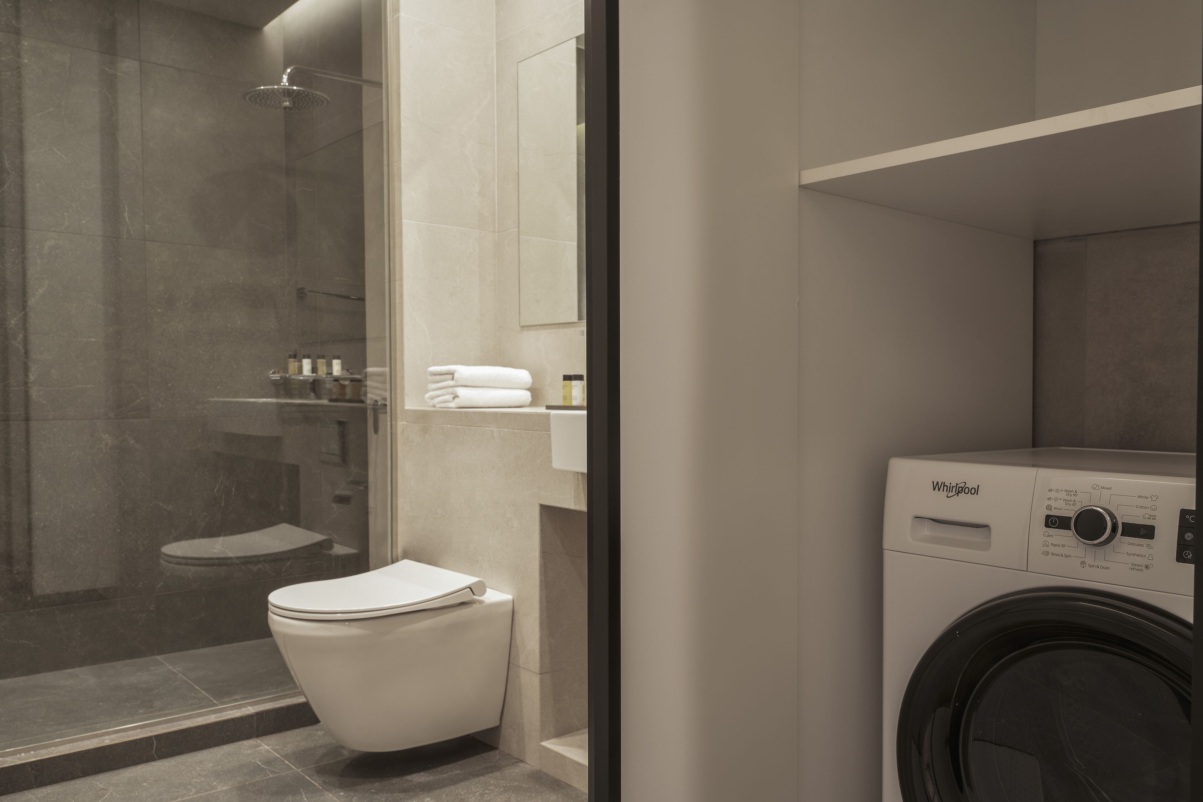 A modern bathroom with a toilet, a glass-enclosed shower, and a Whirlpool washing machine.