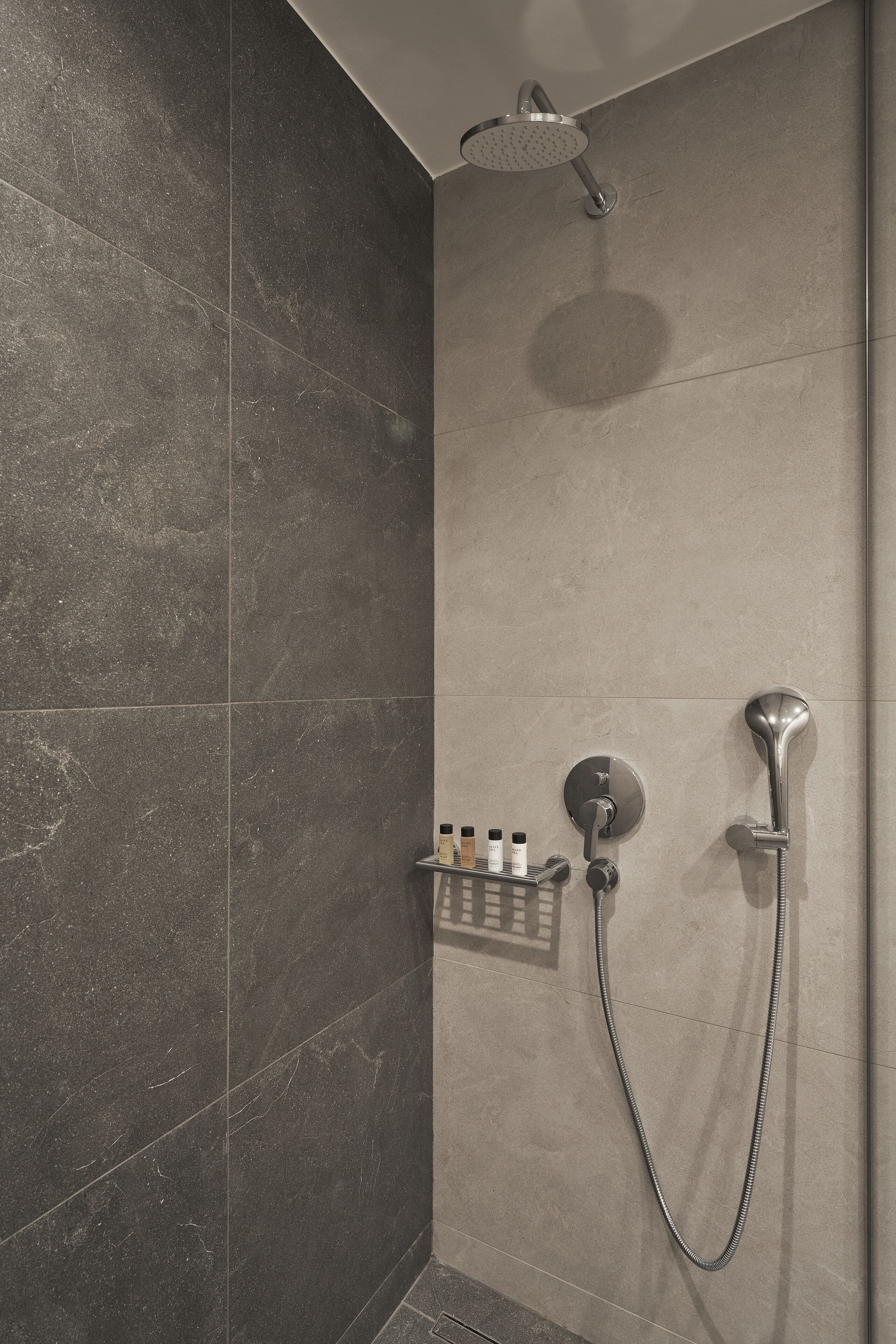 A shower area with a handheld showerhead and a wall-mounted faucet.