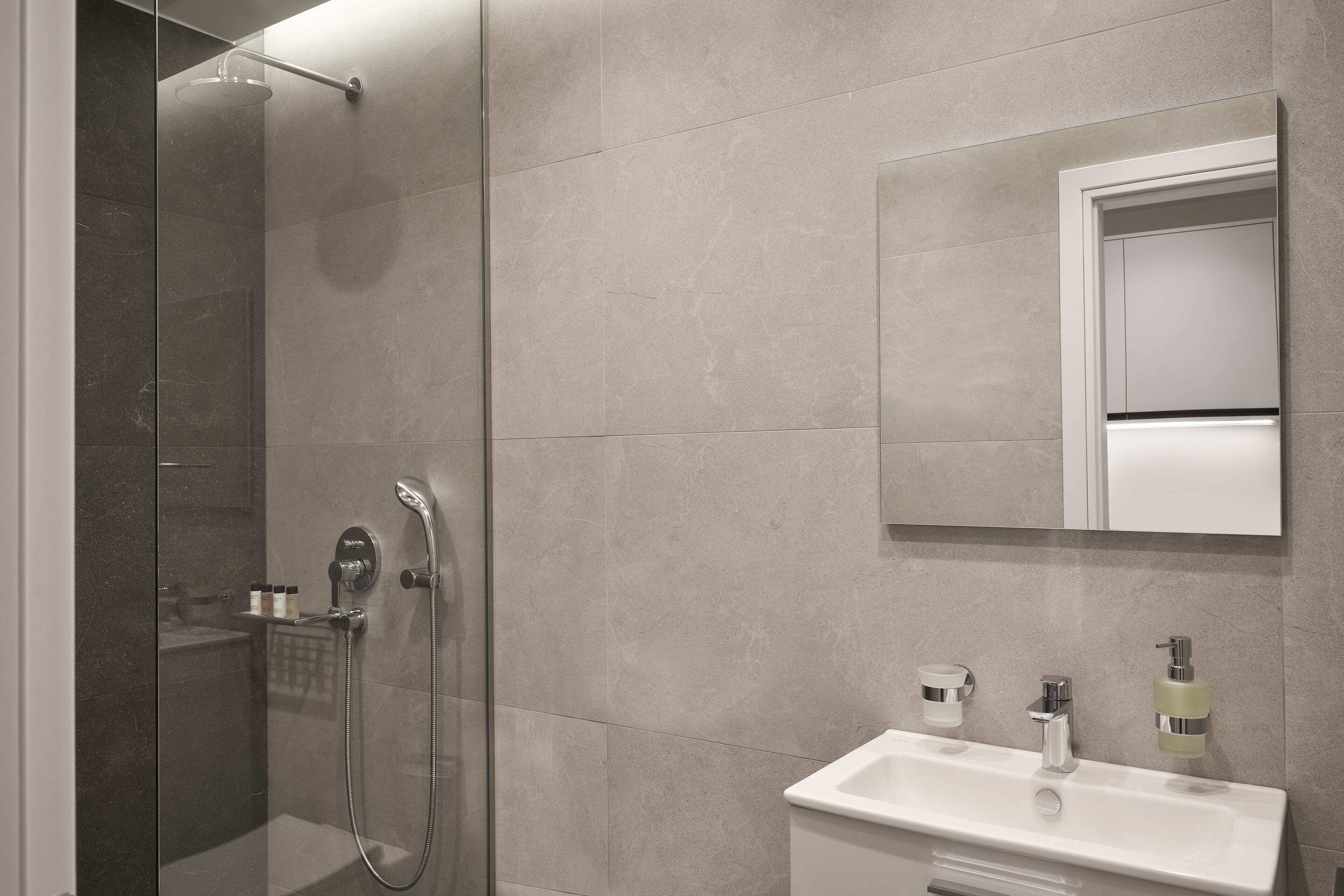 Une salle de bain moderne avec une douche à parois de verre, un lavabo blanc et un miroir au-dessus.