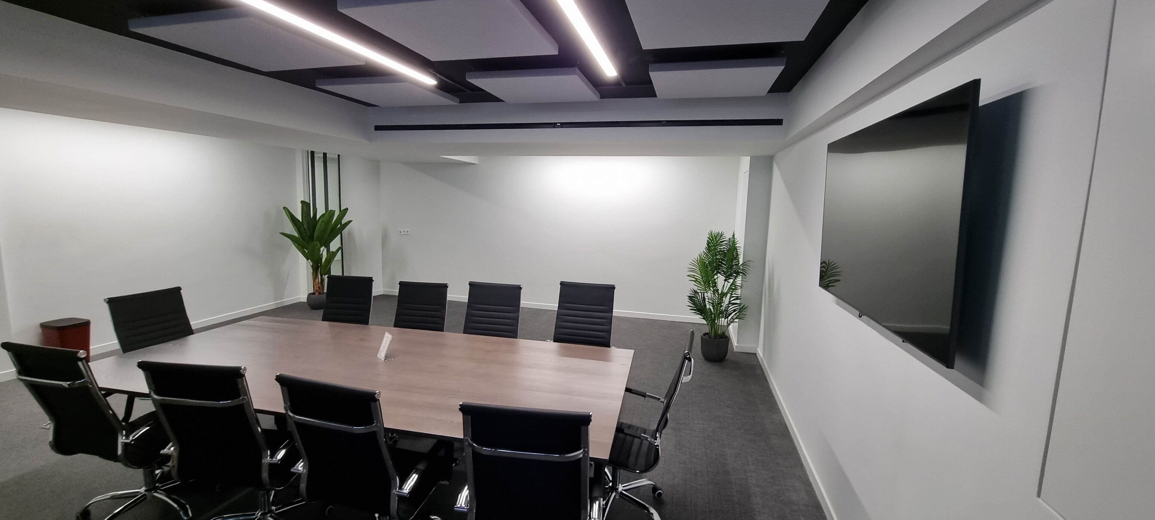 Une salle de conférence avec une longue table, des chaises noires et des plantes en pot.
