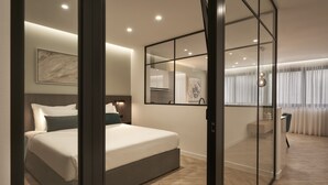 A modern hotel room with a large bed, a glass partition, a desk, and a view of the city. - Hestia - Dimitressa 4 (Athens)